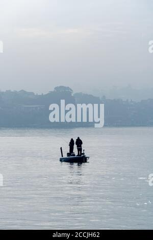 Lors d'un hivers brumeux matin, deux hommes se tiennent dans un Petit bateau de pêche ouvert près de Cockatoo Island pêche avec des cannes dans l'eau tranquille du port Banque D'Images