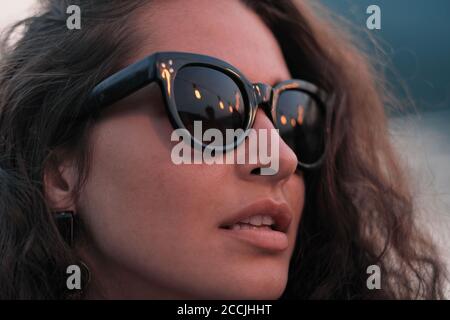 Gros plan de jeune belle femme avec des cheveux bouclés dans des lunettes de soleil debout à l'extérieur Banque D'Images