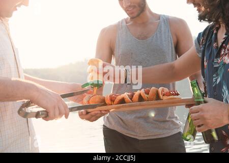 Gros plan de jeunes hommes préparant des hot dogs avec de la sauce pendant la fête à l'extérieur Banque D'Images