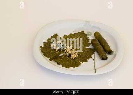 La main est enveloppée, roulant de feuilles de raisin humide dans une assiette blanche, traditionnel Préparation de nourriture turque, vue ci-dessus Banque D'Images