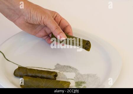 La main est enveloppée, roulant de feuilles de raisin humide dans une assiette blanche, traditionnel Préparation de nourriture turque, vue ci-dessus Banque D'Images