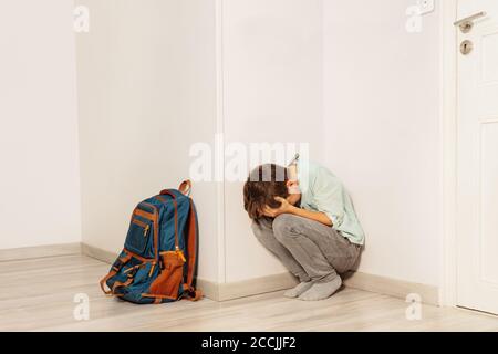 Triste garçon stressé a intimidé dans le cri de l'école assis dans le coin avec sac à dos pour fils Banque D'Images