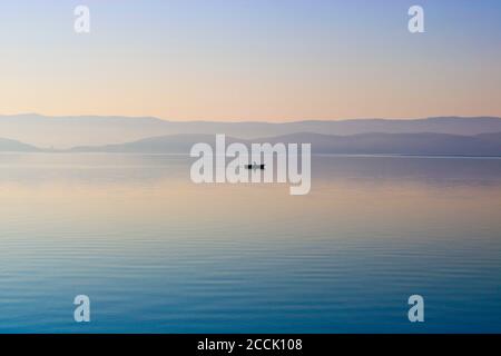 Aube sur la surface de l'eau du lac. Bateau solitaire avec un pêcheur. Eau calme et claire. Turgoyak, Russie. Banque D'Images