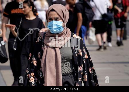 Jeune femme musulmane portant le visage chirurgical couvrant dans la rue animée, Londres, Royaume-Uni. Banque D'Images
