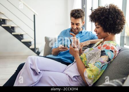 Couple utilisant des smartphones tout en étant assis sur un canapé dans moderne penthouse Banque D'Images