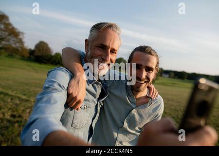 Père heureux avec un fils adulte prenant un selfie sur un prairie dans la campagne Banque D'Images