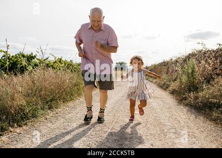 Un homme espiègle qui court avec sa petite-fille sur une route de terre au milieu plantes Banque D'Images