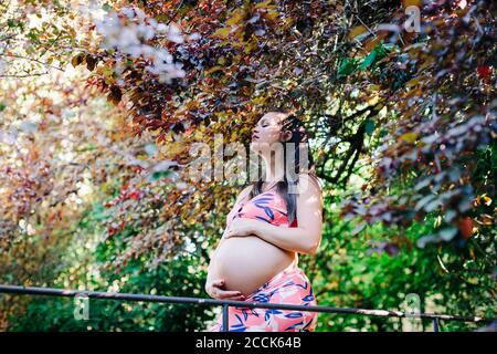 Belle femme enceinte debout avec les yeux fermés par des arbres à stationnement Banque D'Images