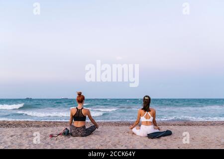 Les jeunes femmes méditant sur la plage contre le ciel clair pendant le coucher du soleil Banque D'Images