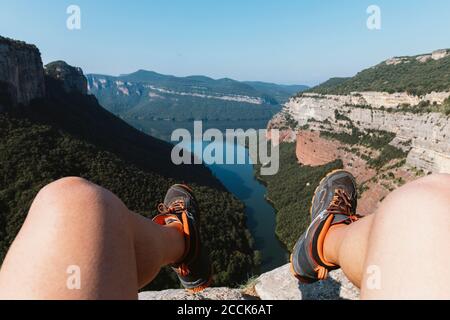 Jambes d'homme assis sur la montagne contre le ciel clair à Vilanova de Sau, Catalogne, Espagne Banque D'Images