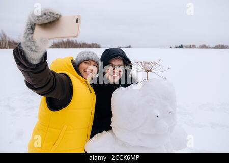 Couple souriant prenant le selfie avec bonhomme de neige Banque D'Images