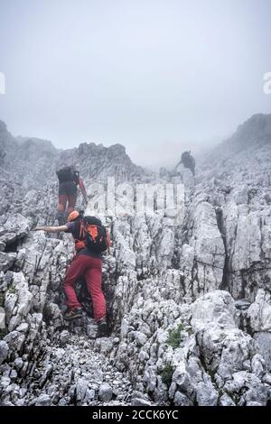 Des randonneurs mâles grimpant sur une montagne rocheuse contre le ciel par temps brumeux, Alpes de Bergamasque, Italie Banque D'Images