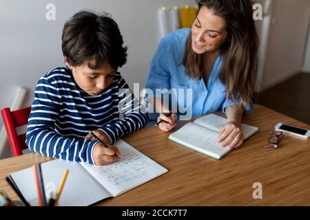 Jeune femme aidant le garçon à écrire des devoirs sur la table à accueil Banque D'Images