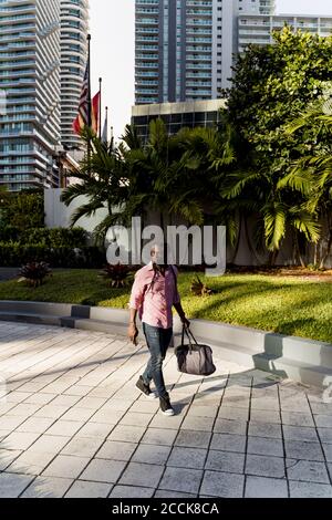 Afro jeune homme avec sac marche sur le sentier de la ville de Miami, Floride, États-Unis Banque D'Images