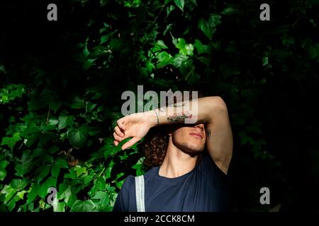 Jeune homme se cachant le visage en se tenant contre les plantes Banque D'Images