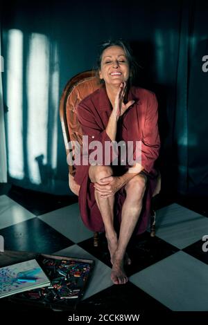 Femme âgée souriante avec les yeux fermés, assise sur la chaise à accueil Banque D'Images