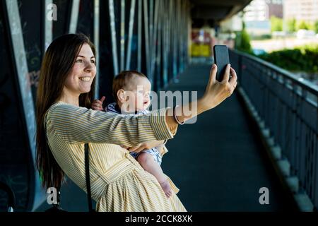 Mère souriante avec son bébé garçon prenant un selfie pont Banque D'Images
