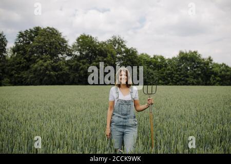 Jeune femme avec fourche de foin debout dans un champ de grain dans la campagne Banque D'Images