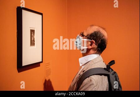 Un homme portant une couverture de visage regarde un dessin d'Aubrey Beardsley sur un fond orange vif. Banque D'Images