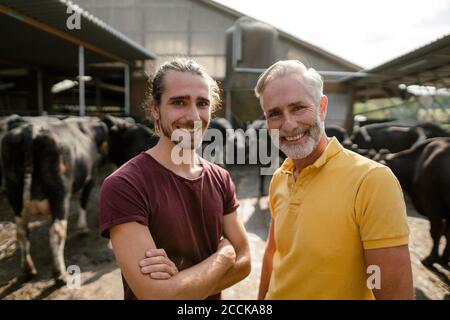 Portrait d'un fermier mûr heureux avec un fils adulte à la vache maison sur une ferme Banque D'Images