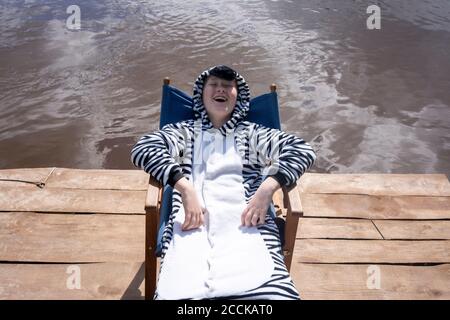 Garçon souriant en costume de zébré assis sur une chaise au bord du lac Banque D'Images