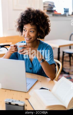 Femme attentionnés tenant une tasse de café tout en étant assise avec un ordinateur portable à café-restaurant Banque D'Images