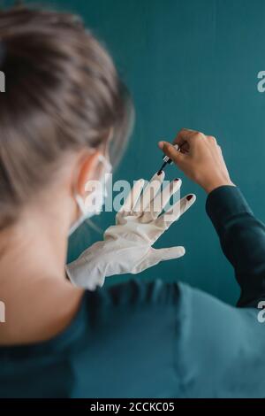 Jeune femme appliquant du vernis à ongles sur un gant de protection Banque D'Images