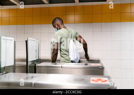 Jeune homme portant un masque avec sac à dos marchant à travers le tourniquet à station de métro Banque D'Images