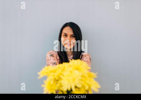 Jeune femme offrant des fleurs tout en se tenant contre le mur Banque D'Images