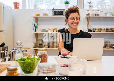 Femme souriante utilisant un ordinateur portable sur l'île de cuisine à l'école de cuisine Banque D'Images