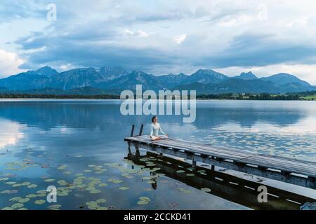 Femme méditant en étant assise sur la jetée au-dessus du lac contre les montagnes Banque D'Images