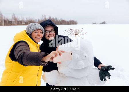 Couple souriant prenant le selfie avec bonhomme de neige Banque D'Images