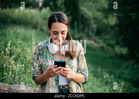 Message de femme souriante depuis un smartphone au parc Banque D'Images
