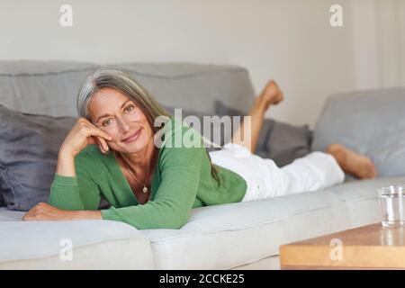 Femme souriante couchée sur un canapé à la maison Banque D'Images