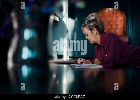 Femme âgée qui dessine dans un livre en étant couché sur le sol accueil Banque D'Images