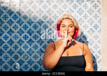 Femme montrant le signe de silence avec le doigt sur les lèvres contre le mur Banque D'Images