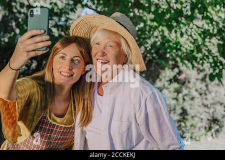 Femme de taille moyenne souriante prenant un selfie avec une mère dans la cour Banque D'Images