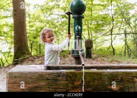 Jolie fille jouant avec une fontaine contre les arbres dans la forêt Banque D'Images