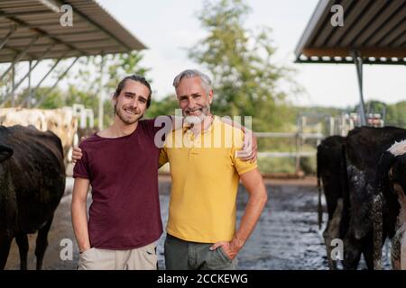 Portrait d'un fermier mûr heureux et d'un fils adulte qui s'embrasse à maison de vache sur une ferme Banque D'Images