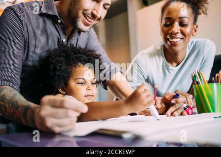 Parents souriants regardant bébé fille dessin sur papier à accueil Banque D'Images