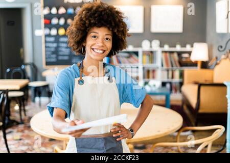 Bonne femme propriétaire qui donne le menu tout en se tenant à la main branché au café-restaurant Banque D'Images