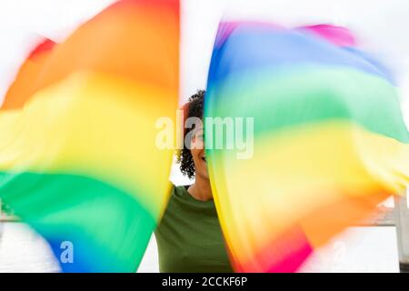 Gros plan d'une femme adulte de taille moyenne qui agite des drapeaux arc-en-ciel debout en ville Banque D'Images