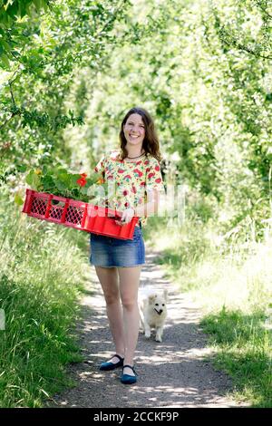 Jeune femme souriante portant du nasturtium dans un panier tout en restant debout ferme Banque D'Images