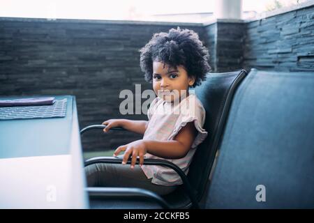 Petite fille mignonne avec cheveux bouclés assis sur une chaise accueil Banque D'Images