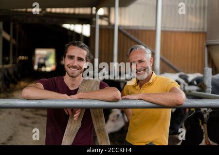 Portrait d'un fermier mûr souriant avec un fils adulte à la vache maison sur une ferme Banque D'Images