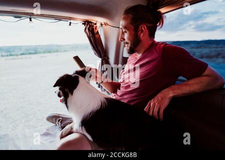 Homme souriant utilisant le téléphone par chien dans la maison de moteur Banque D'Images