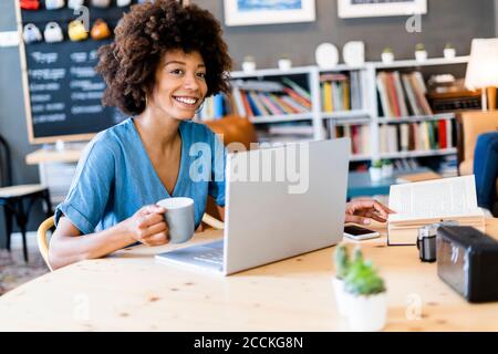 Femme attentionnés tenant une tasse de café tout en étant assise avec un ordinateur portable à table basse Banque D'Images