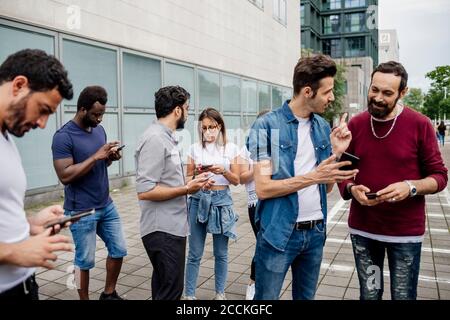 Des amis qui parlent et utilisent des smartphones tout en étant debout sur une piste de marche en ville Banque D'Images