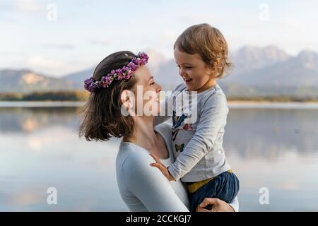 Mère souriante portant une tiara portant sa fille tout en se tenant contre le lac Banque D'Images