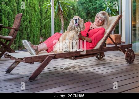 Femme âgée élégante avec chien se détendant sur une chaise longue patio Banque D'Images